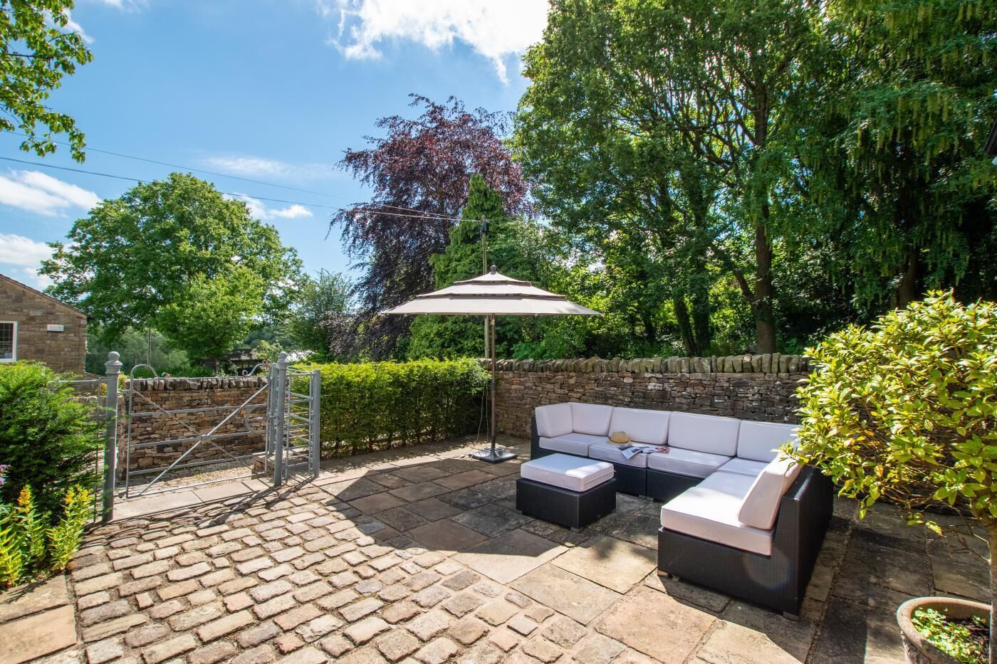 Eine Terrasse mit Steinboden, einem Metallgitter, einem weißen Sonnenschirm und einem schwarz-weißen Sofa.