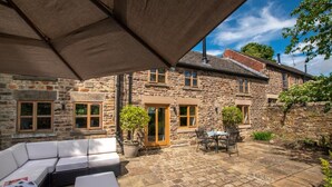 Ein Steinhaus mit Terrasse, Sitzgelegenheiten im Freien und einem kleinen Tisch.