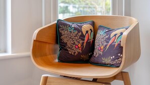 Une chaise en bois agrémentée de deux coussins décoratifs aux motifs d’oiseaux et de fleurs.