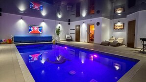Una piscina con iluminación LED, una pantalla de televisión y un área de descanso con asientos.