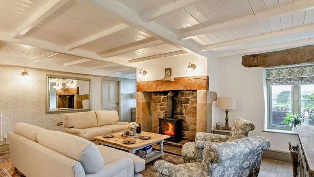 A cozy living room with a stone fireplace, a sofa, a patterned armchair, and a large mirror. - 4 Bed in Skipton (oc-95155) (Thorpe)