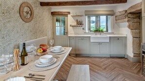A kitchen with a dining table set for a meal, a clock on the wall, and a view of the outdoors through the window. - 4 Bed in Skipton (oc-95155) (Thorpe)