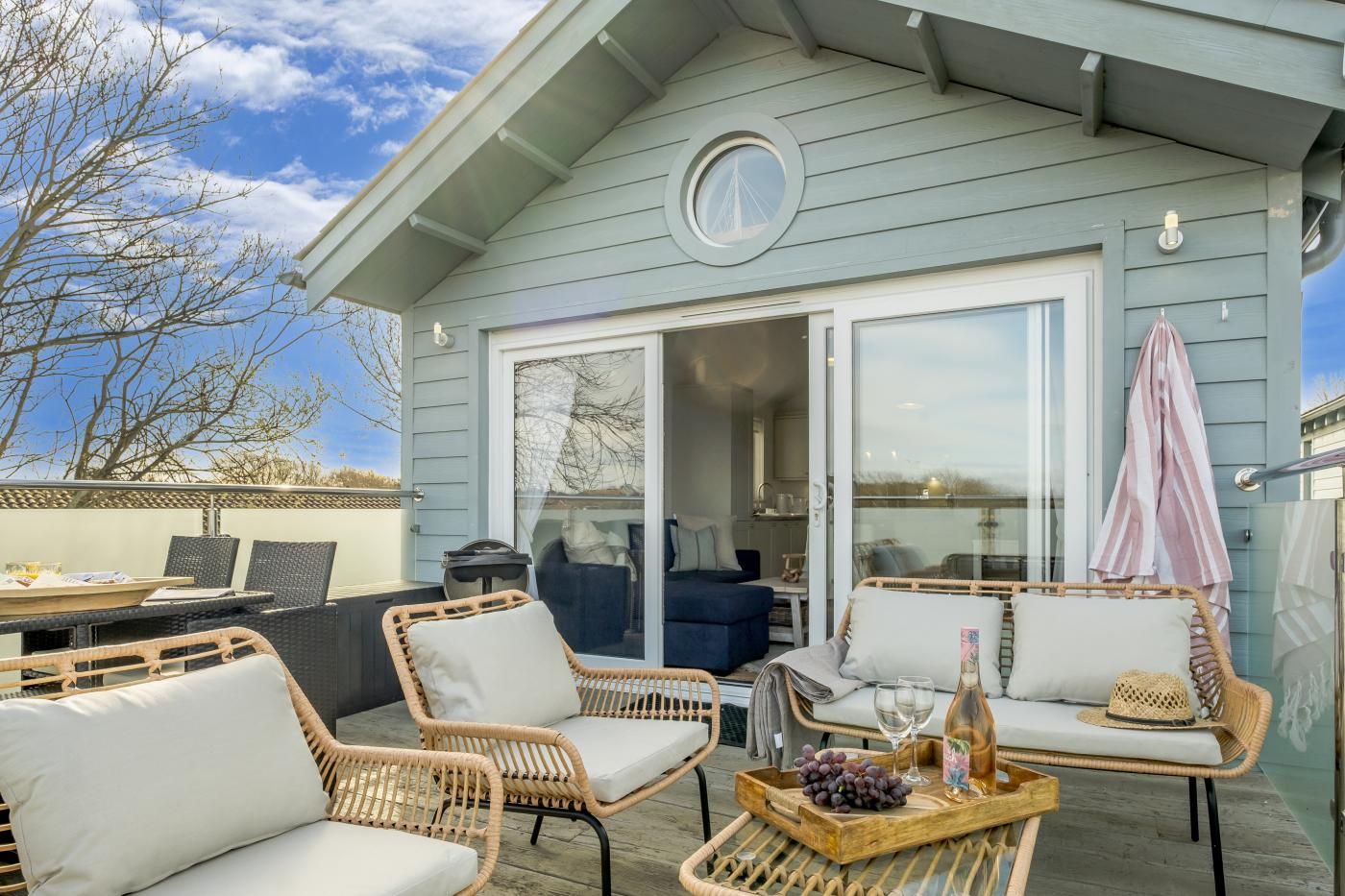 A covered outdoor seating area with wicker furniture, a dining table, and a glass door leading to an interior space.