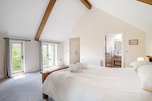 A bedroom with a large bed, a window, a door leading to a bathroom, and a view of greenery outside.