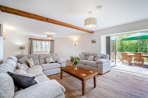 Een ruime woonkamer met een grote zithoek, een houten salontafel en een eethoek met buitentoegenstelling.