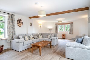Een ruime woonkamer met een grote grijze modulaire bank, een houten salontafel en een houten vloer.