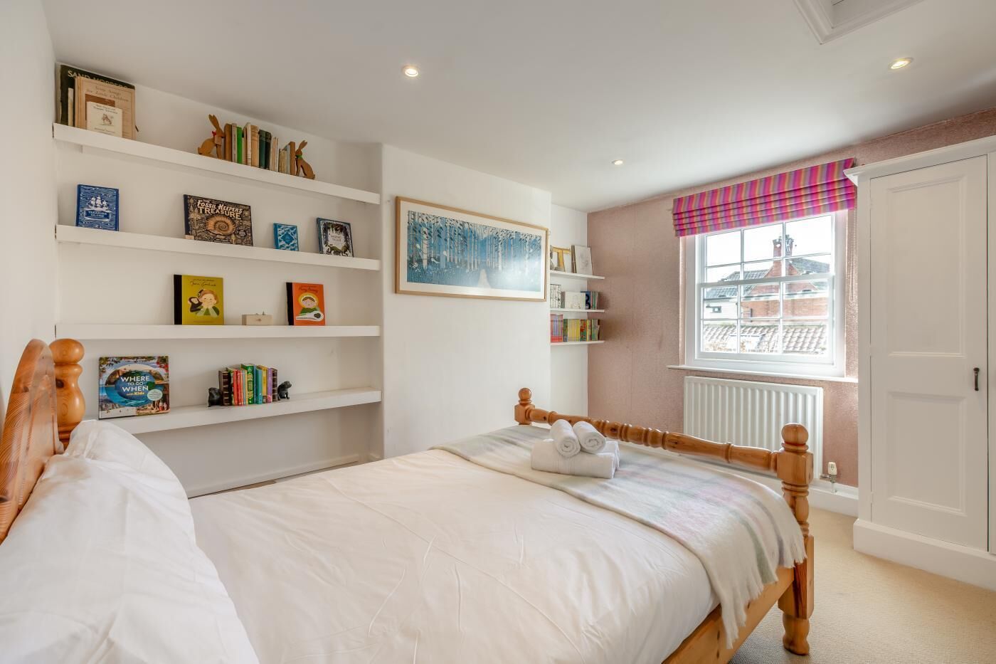 A bedroom with a bed, white walls, a bookshelf, a window with a view, and a door.