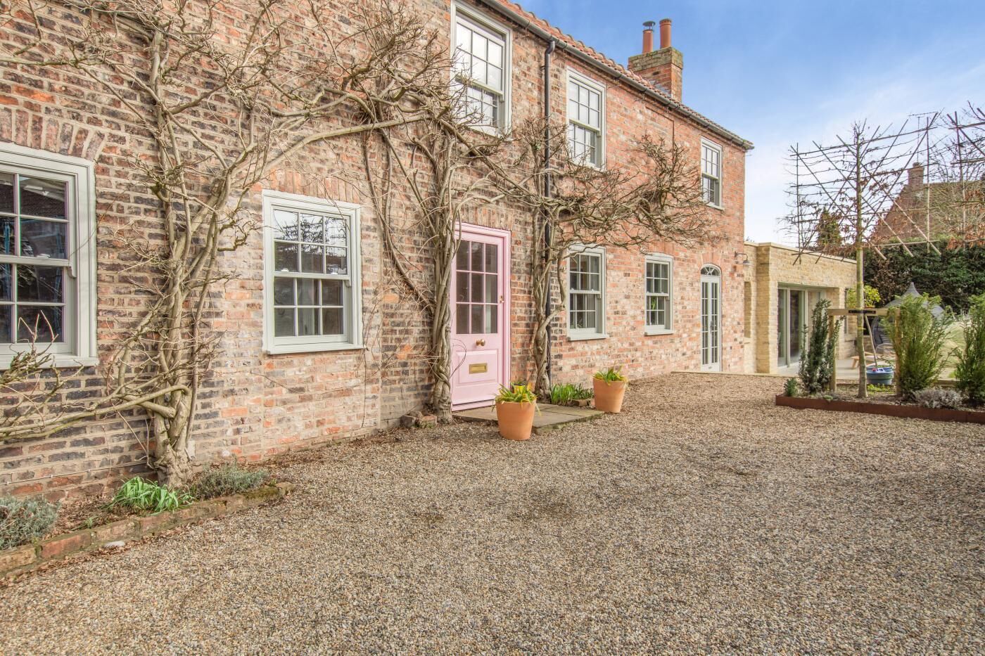 A brick house with a gravel driveway, a pink door, and potted plants.