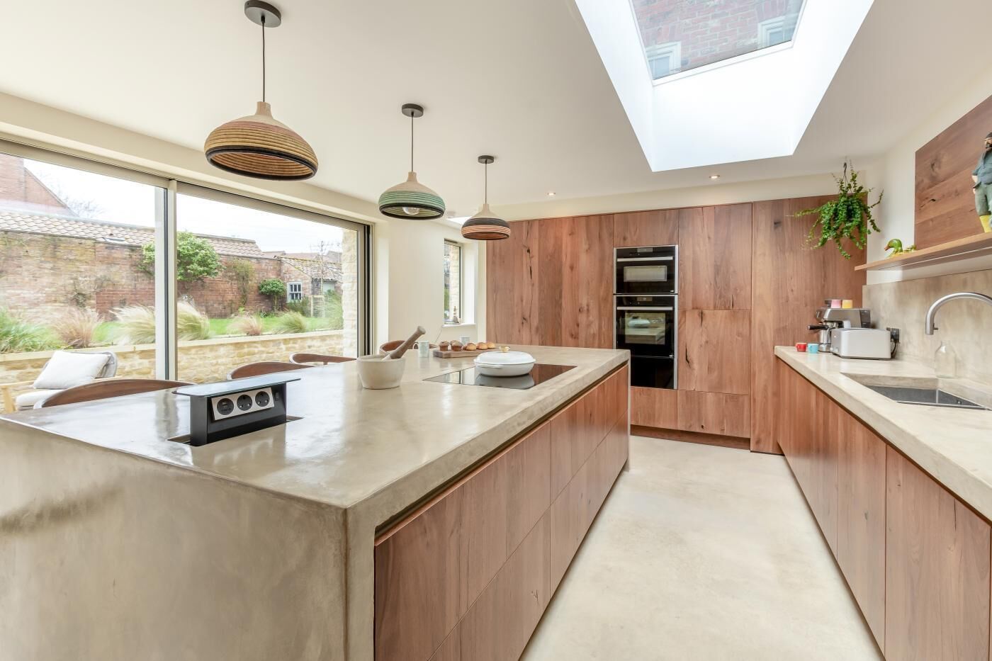 Une cuisine moderne dotée d’un grand îlot central, de meubles en bois, d’une lucarne et d’une vue sur le jardin arrière.