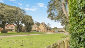 A grassy area with a wooden fence, a stone building, and trees. - 2 Bed in Holkham (oc-c34779) (Holkham)