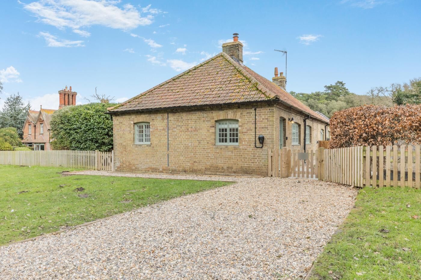 A small stone building with a tiled roof, a gravel driveway, and a wooden fence.
