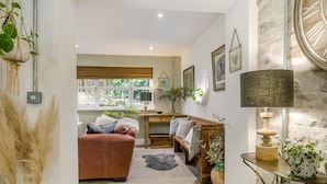 A cozy living room with a leather sofa, a wooden bench, a dining table, and a large window with a view of greenery. - 3 Bed in Ellwood (oc-t35963) (Ellwood)