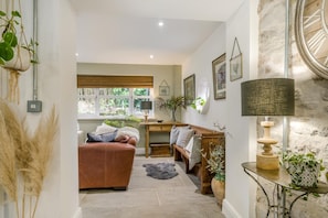 A cozy living room with a leather sofa, a wooden bench, a dining table, and a large window with a view of greenery. - 3 Bed in Ellwood (oc-t35963) (Ellwood)