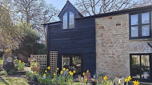 A modern house with a dark exterior, stone walls, and a garden with daffodils. - 3 Bed in Ellwood (oc-t35963) (Ellwood)