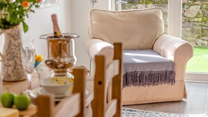 Beigenvärinen nojatuoli, jossa on kuviollinen huopa, puinen tuoli, pöytä, jossa on kuparinen ruukku, ja maljakko, jossa on kukkia.