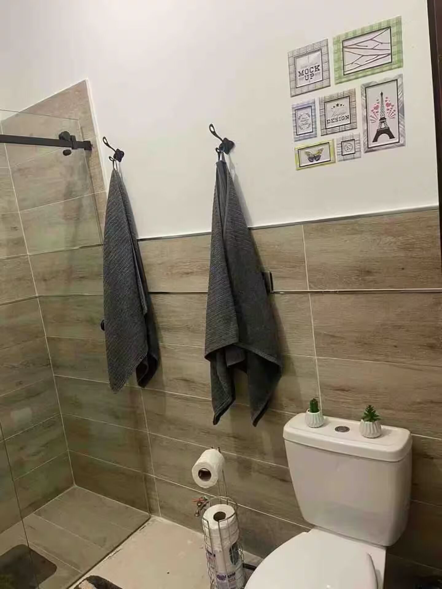 A bathroom with a toilet, a towel rack with two towels, a toilet paper holder, and a wall with framed pictures.