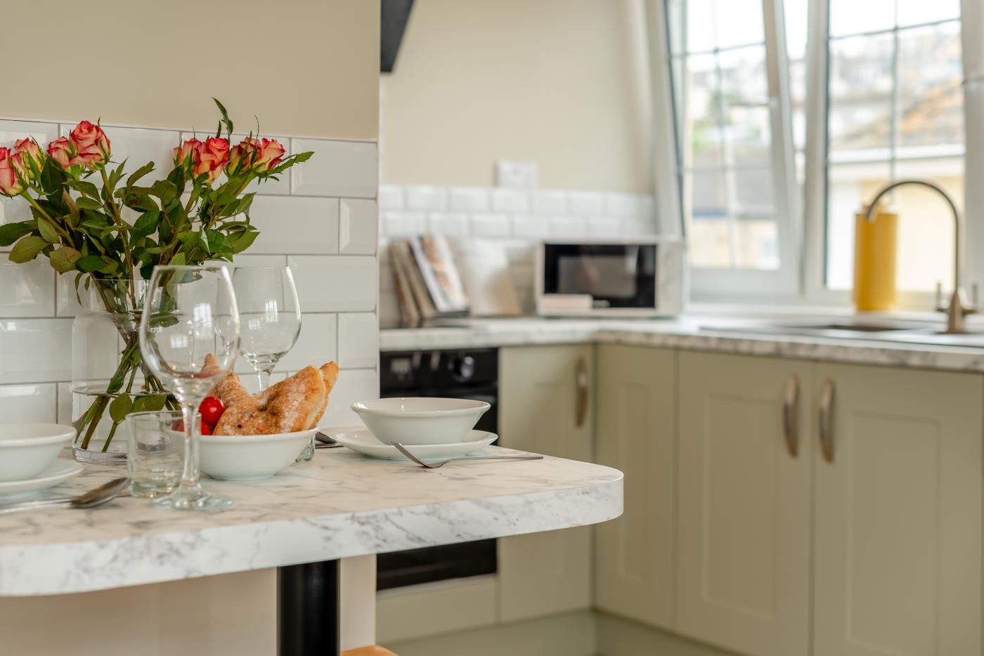 Un plan de travail de cuisine avec un vase de fleurs, un verre de vin et un panier de pain.