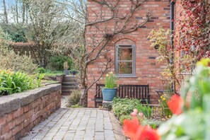 A brick building with a window, a bench, and a pathway leading to a door. - 4 Bed in Shrawley (oc-s34861) (Shrawley)