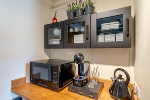 A kitchen with a microwave, coffee maker, kettle, and cabinets labeled 'Bread' and 'Biscuits'.