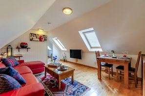 A loft-style living room with a red sofa, a wooden dining table, and a TV.