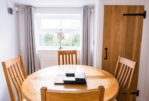 A dining area with a round wooden table, two wooden chairs, a globe decoration, and a window with curtains. - 2 Bed in Shaldon (oc-t36353) (Shaldon)