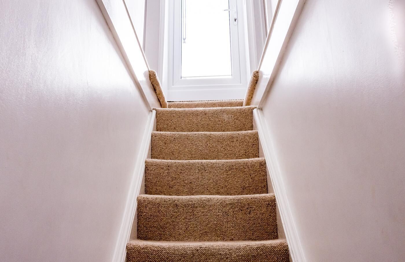 A carpeted staircase with white walls and a door at the top.