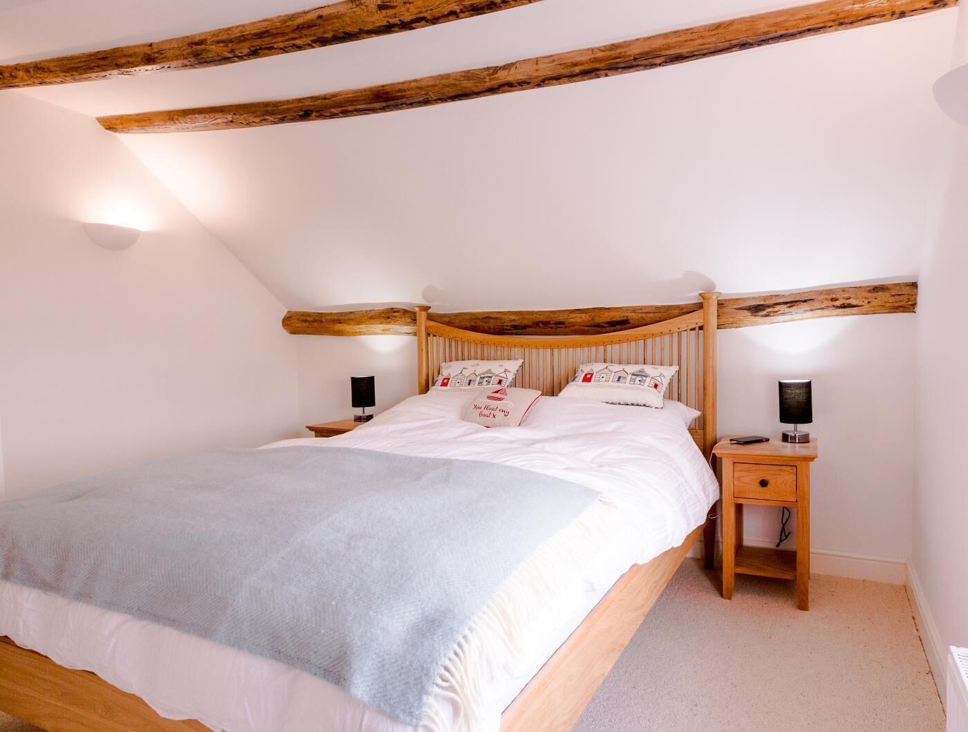 A bedroom with a wooden bed frame, white bedding, two bedside lamps, and a small wooden nightstand with a lamp.