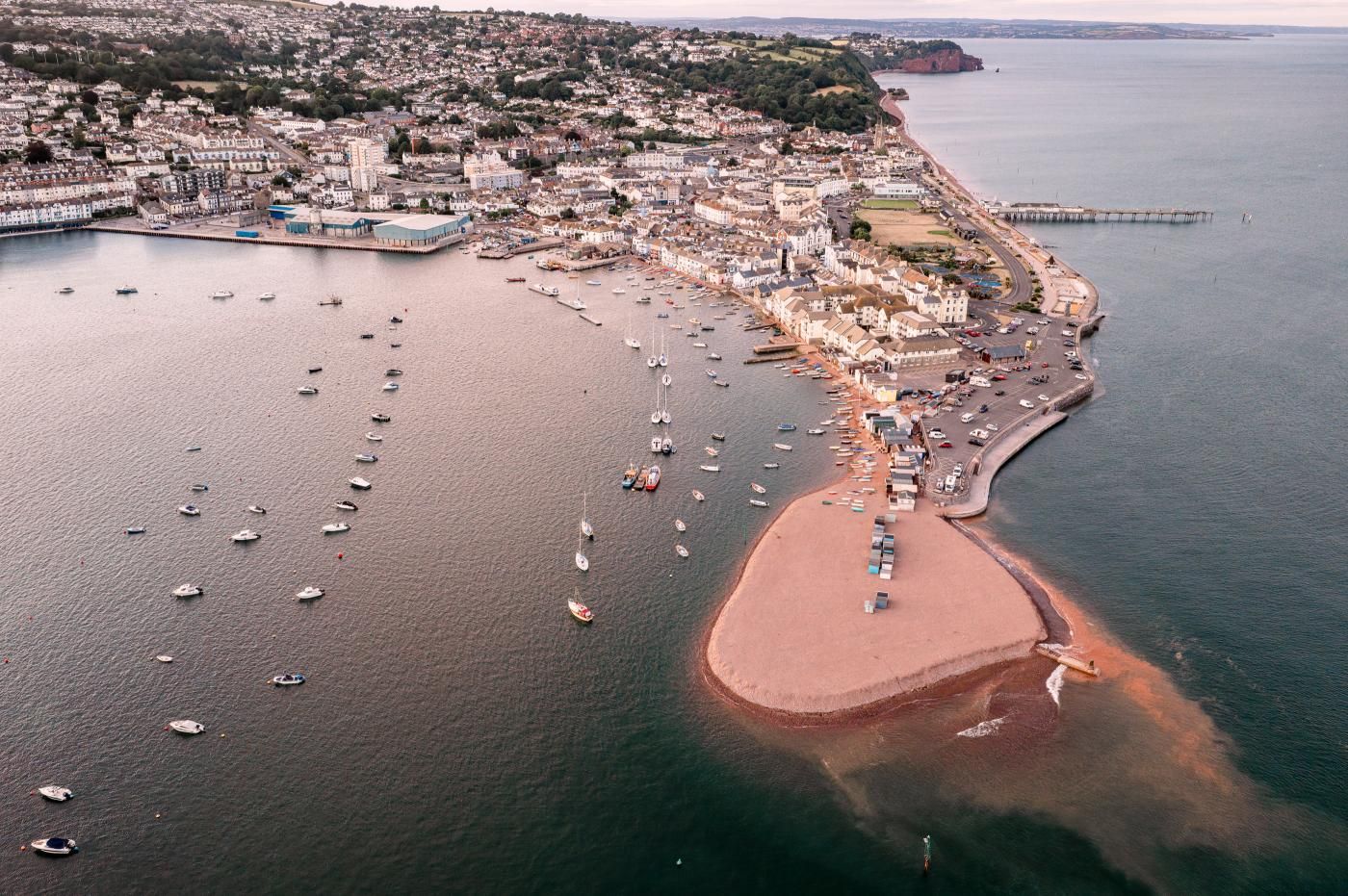 Vista aèria d'una població costanera amb un port esportiu, edificis residencials i una línia de costa corbada.