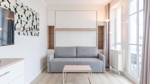 A modern living room with a grey sofa, a wooden coffee table, and a wall-mounted abstract art piece. - Perfekt fur Zwei - Moderne Fewo mit Balkon in Sellin (Sellin)