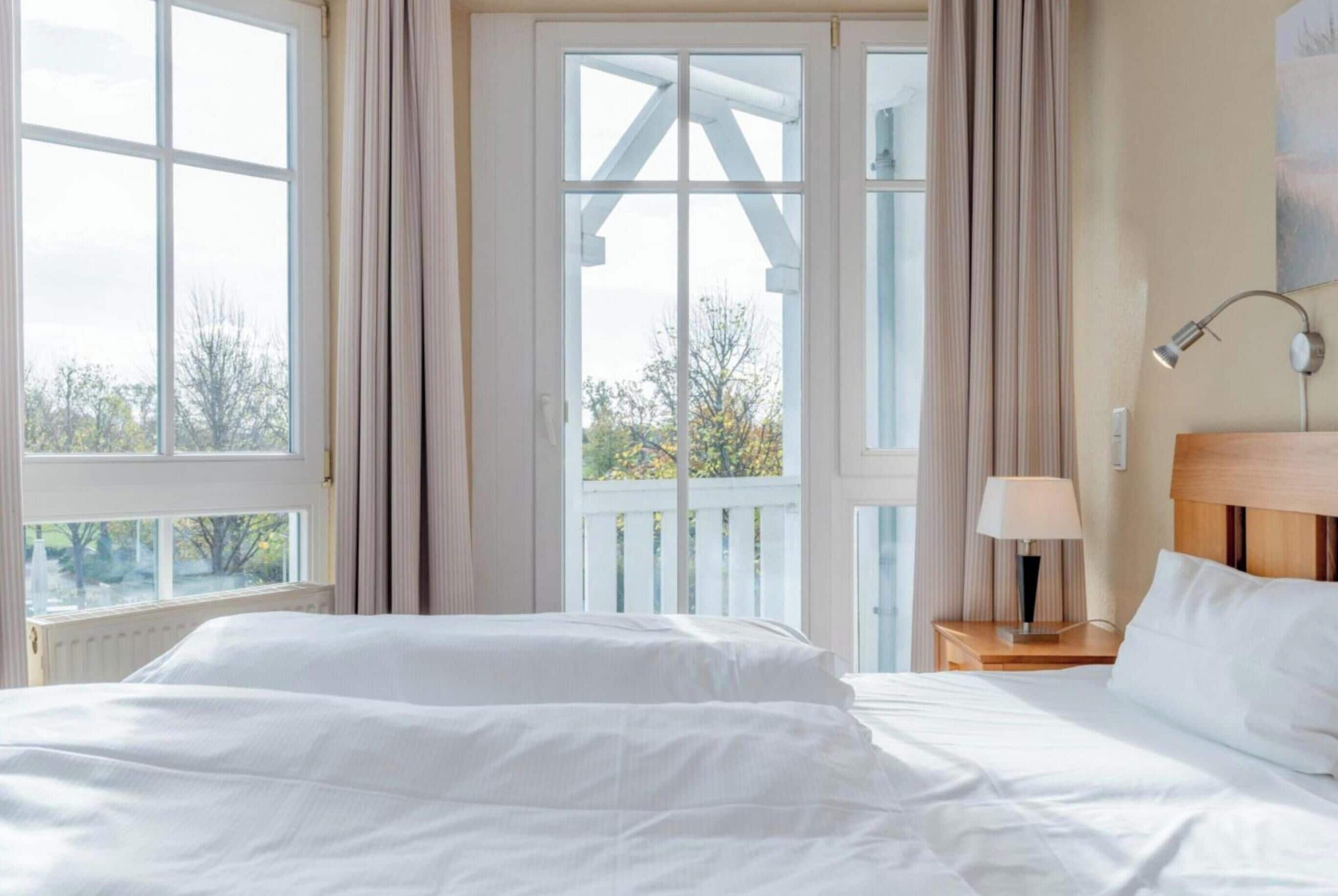 Une chambre à coucher avec un lit, une table de chevet avec une lampe, une fenêtre avec des rideaux et une vue sur les arbres à l’extérieur.