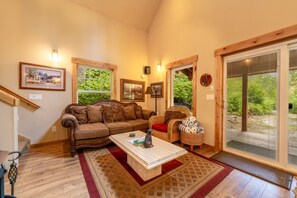 A cozy living room with a sofa, a chair, a coffee table, and a large sliding glass door leading to a garden.