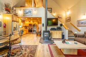 A spacious living area with a high ceiling, a fireplace, a dining table with chairs, a sofa, and a television.