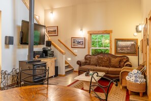 Una sala acogedora con chimenea, un sofá, una mesa de comedor y una escalera.