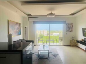 Uma sala moderna com sofá, mesa de centro e vista para uma varanda com paisagem urbana.