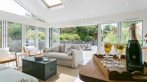 A spacious room with a sofa, a wooden table with glasses and a bottle, and large windows.