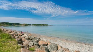 A coastal landscape with a rocky shoreline, calm sea, and distant hills.