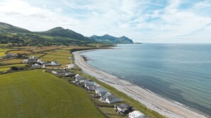 A coastal village with houses along the shoreline, a clear sky, and mountains in the background. - Beach Bungalow - sleeps 6 guests  in 3 bedrooms (Nefyn)