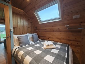 A cozy room with a bed, pillows, a checkered blanket, a skylight, and wooden walls.