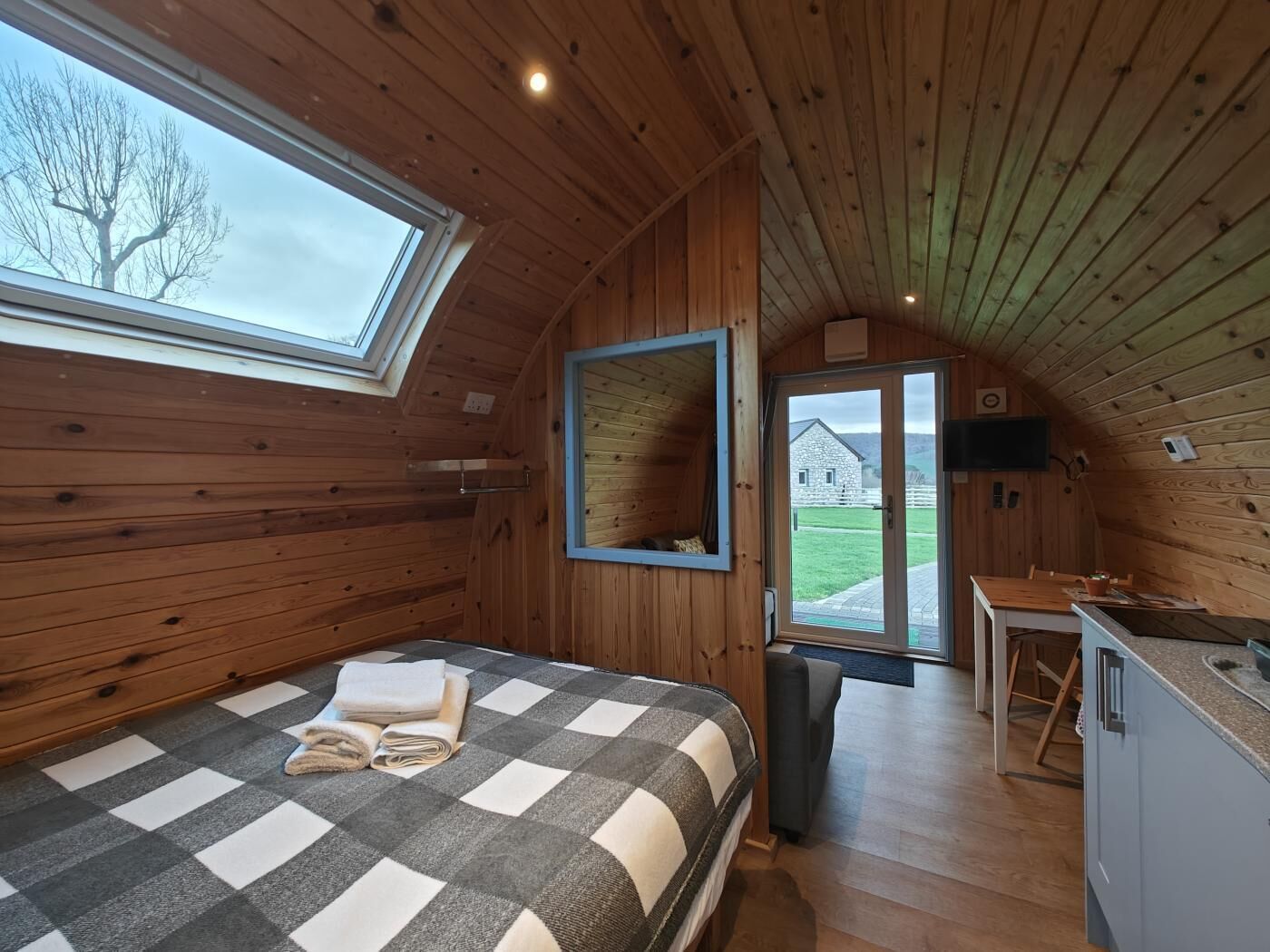 Un chalet confortable avec un lit à carreaux, un coin repas et une grande fenêtre donnant sur un champ verdoyant.