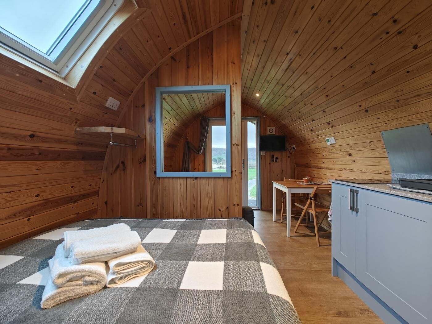 Une chambre mansardée chaleureuse, avec un tapis à carreaux, un lit agrémenté de serviettes roulées, un plafond en bois et un téléviseur.