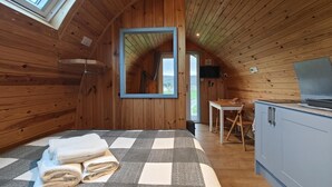 Un dormitorio acogedor en el ático con alfombra a cuadros, una cama con toallas enrolladas, techo de madera y un televisor.