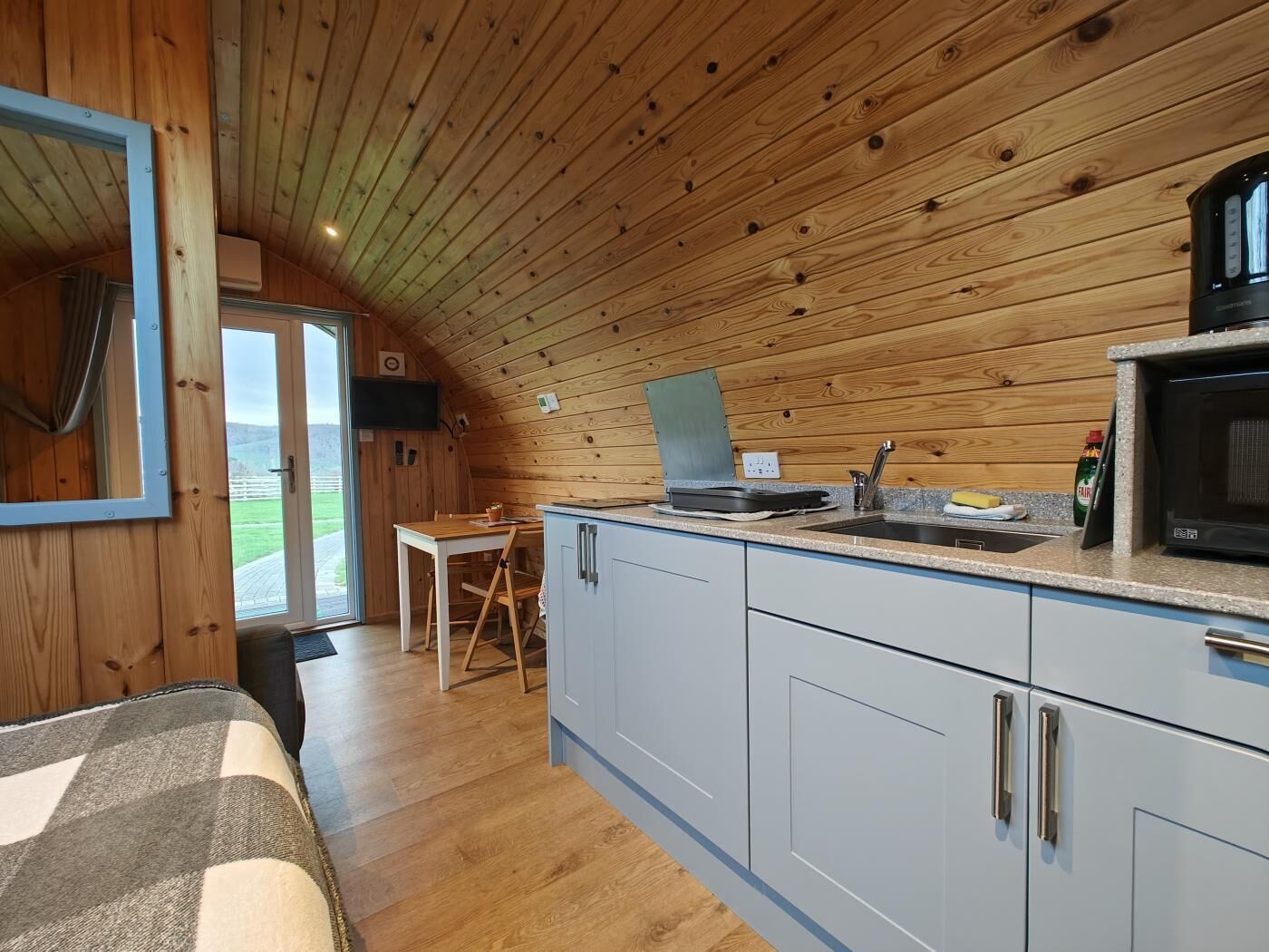 A compact kitchen with wooden walls, a dining area, and a view through a glass door.