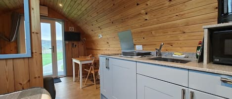 A compact kitchen with wooden walls, a dining area, and a view through a glass door.