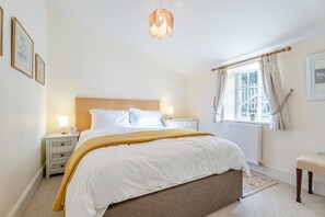 Une chambre à coucher avec un lit, des tables de chevet, une fenêtre avec des rideaux, un radiateur et un luminaire suspendu.