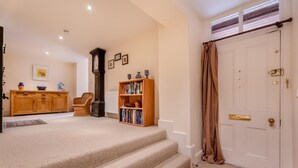 Una escalera alfombrada que conduce a una puerta blanca con una cortina marrón, una estantería de madera, una silla de mimbre y un mueble de madera con adornos.