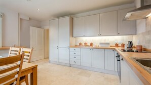 Una cocina moderna con armarios blancos, una mesa de comedor de madera con sillas y un horno empotrado.