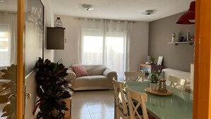 A living room with a sofa, a dining table, and chairs, a large potted plant, and a TV mounted on the wall. - La Mota Beach House with Pool & BBQ (Cubelles)