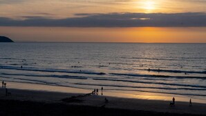 Eine Strandansicht mit Menschen, die spazieren gehen und Fahrrad fahren, und einem Sonnenuntergang über dem Meer.