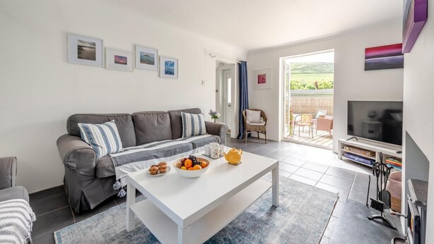 Ein modernes Wohnzimmer mit Sofa, Couchtisch mit Früchten, Fernseher und Blick ins Freie.