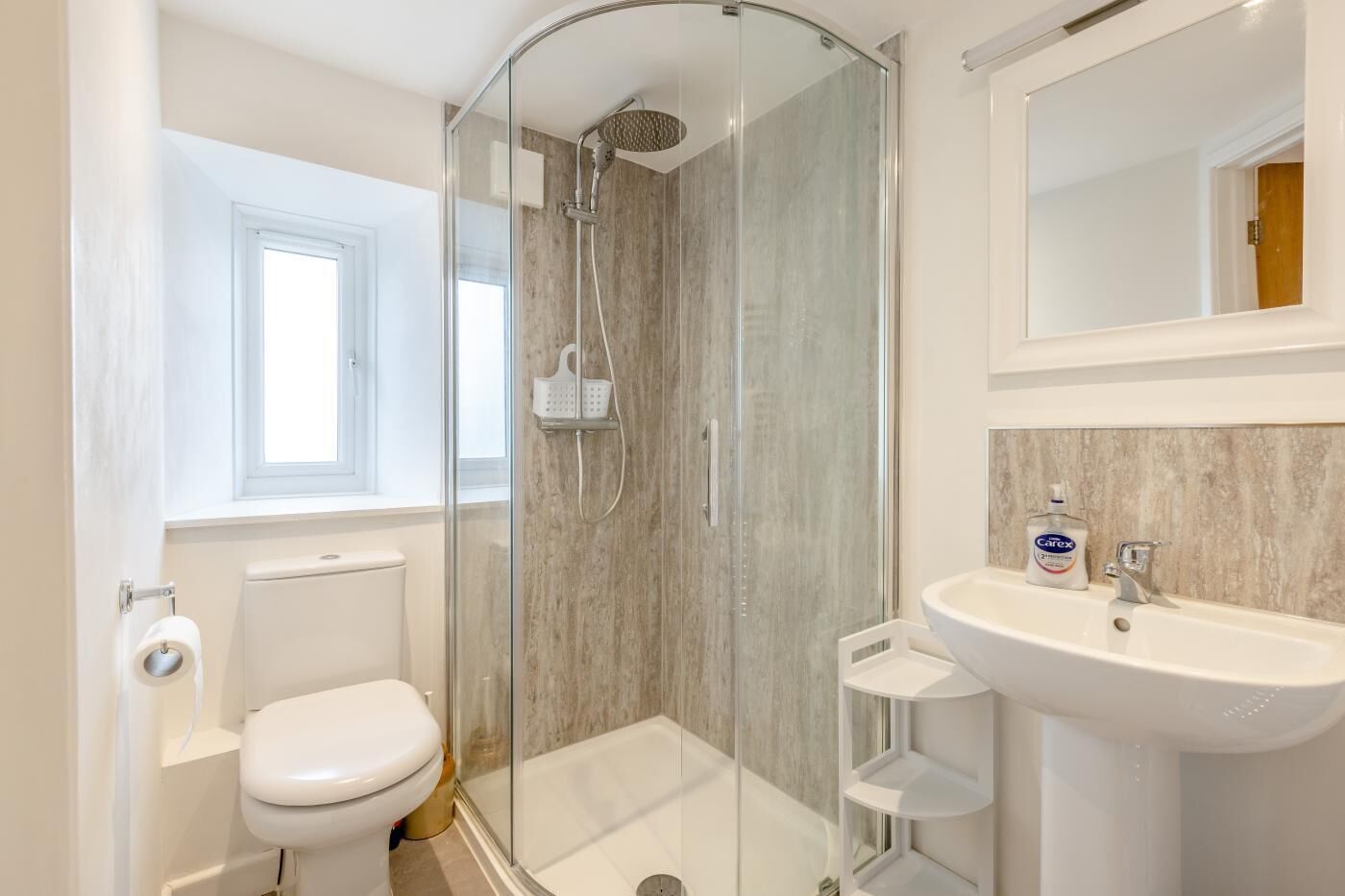 Une salle de bain avec une douche à parois de verre, des toilettes, un lavabo et une fenêtre.